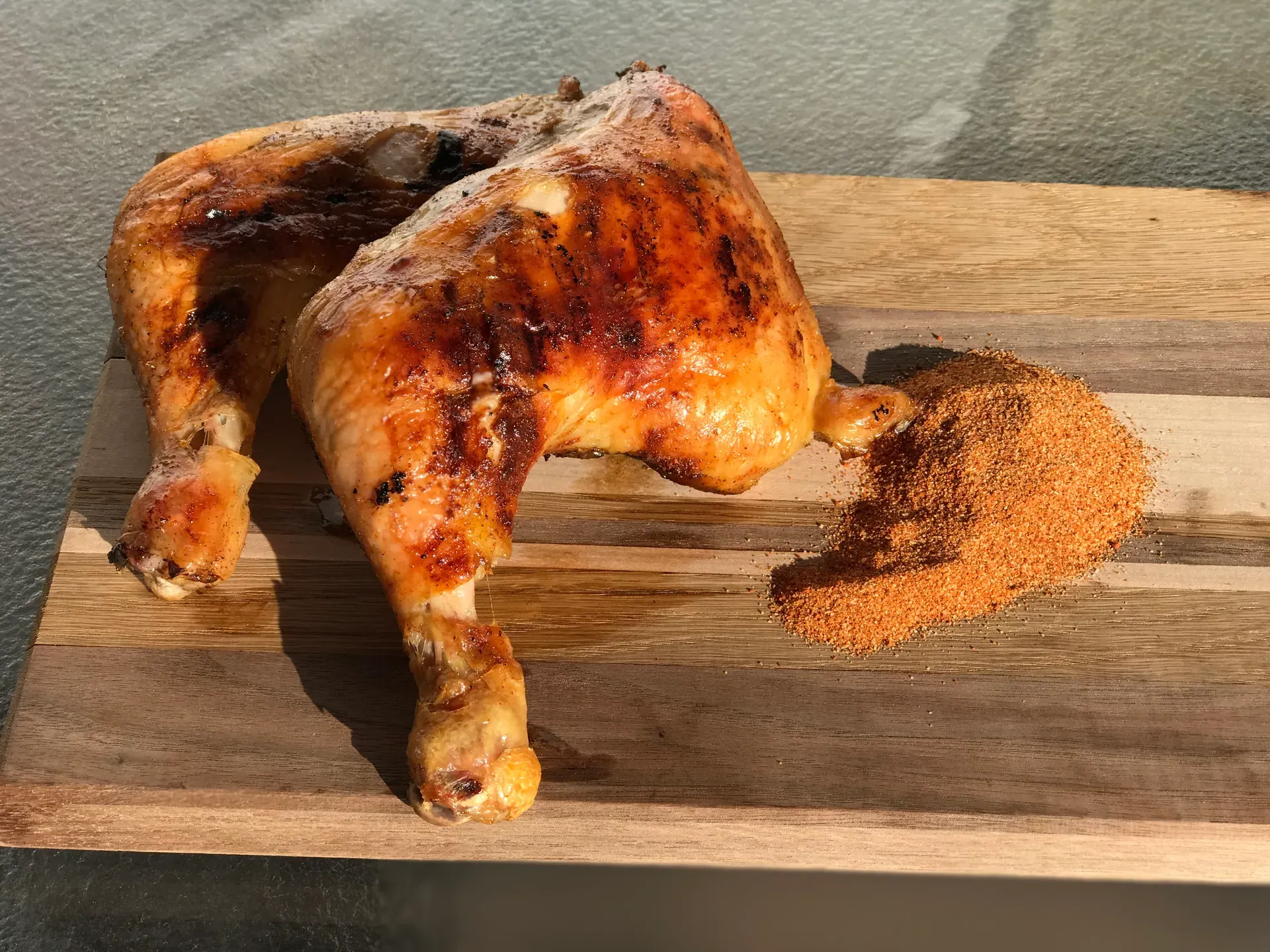 Two smoked BBQ chicken leg quarters from The Pitmaster’s Secret with a pile of the champion dry rub on a wooden board
