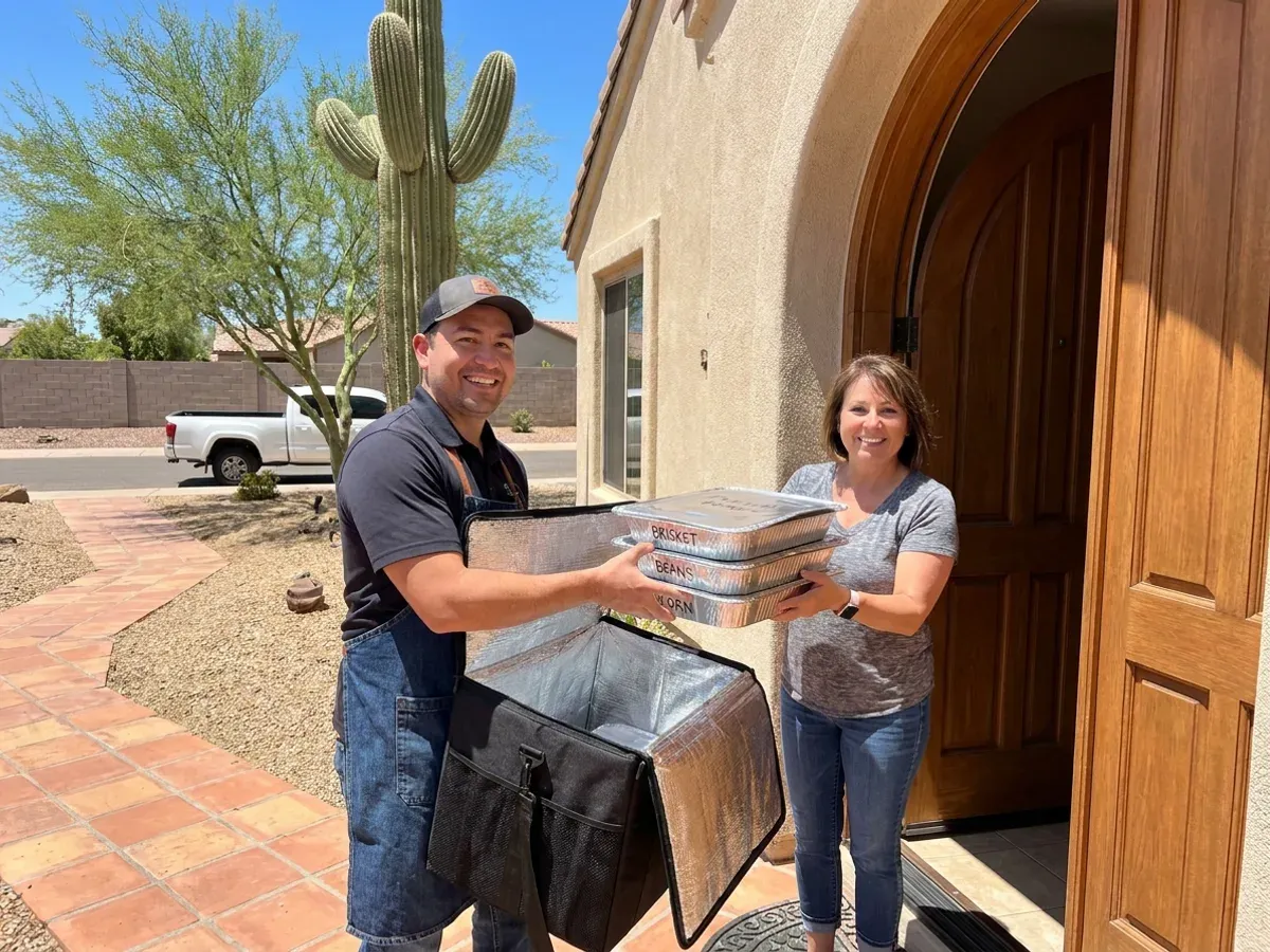 The Pitmaster's Secret caterer handing off labeled foil catering pans to a customer at the front door of an Arizona home