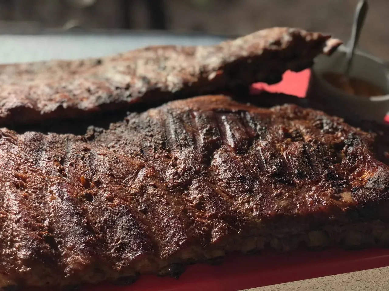Close-up of finished Texas-style baby back ribs on the serving platter, sauce cup on the side