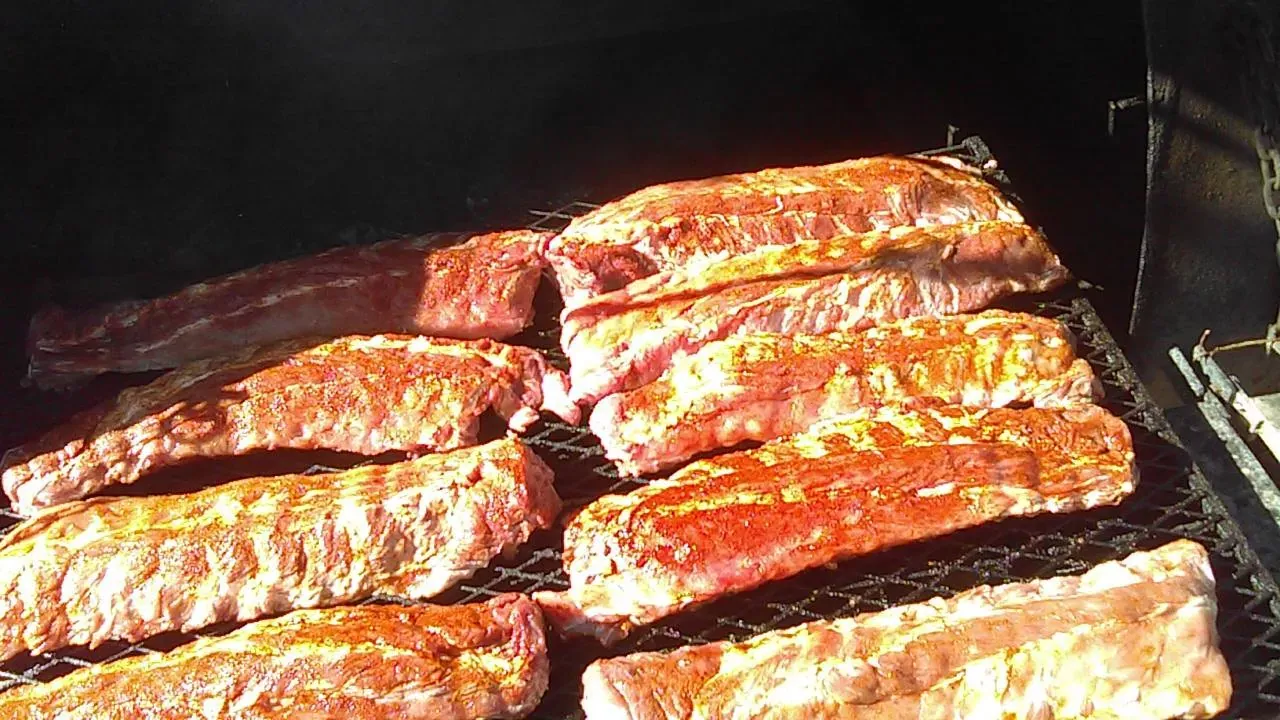 Racks of seasoned ribs filling the smoker grate at a Pitmaster’s Secret cookout
